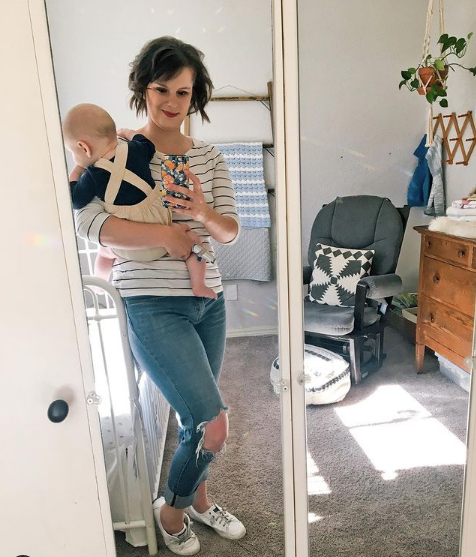 woman standing in a nursery holding a 6 month old baby
